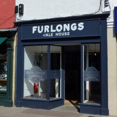 An image of Furlongs Ale House, Preston Street, Faversham. It has a navy front with two glass windows.